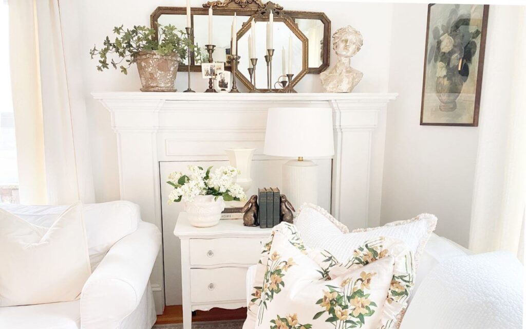 White fireplace mantel styled with gold antique mirrors with brass candelabras and vintage photos.