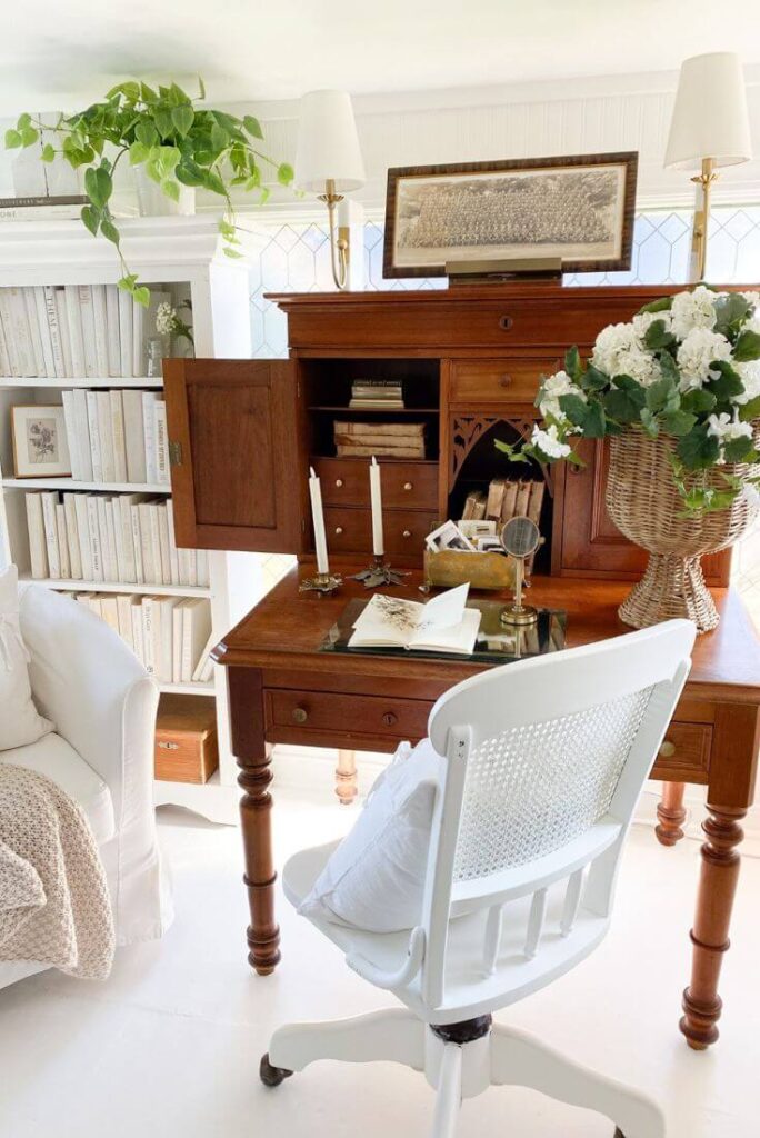 Home library created in a bright sunroom using vintage furniture and simple storage