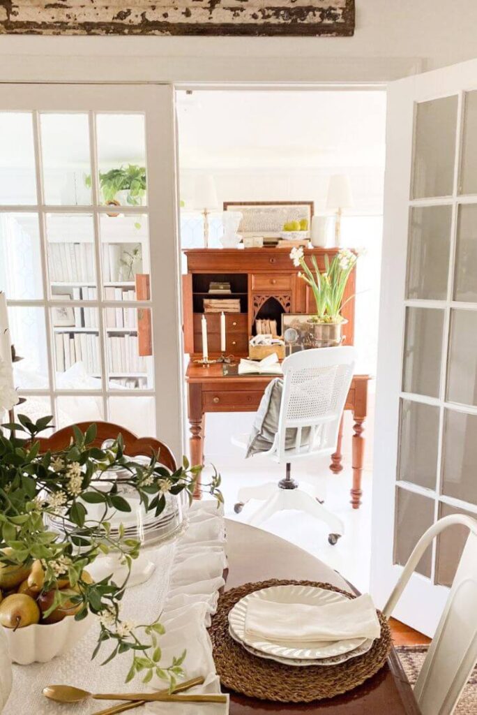 Small sunroom office styled with an antique desk, bookcases, and filtered natural light