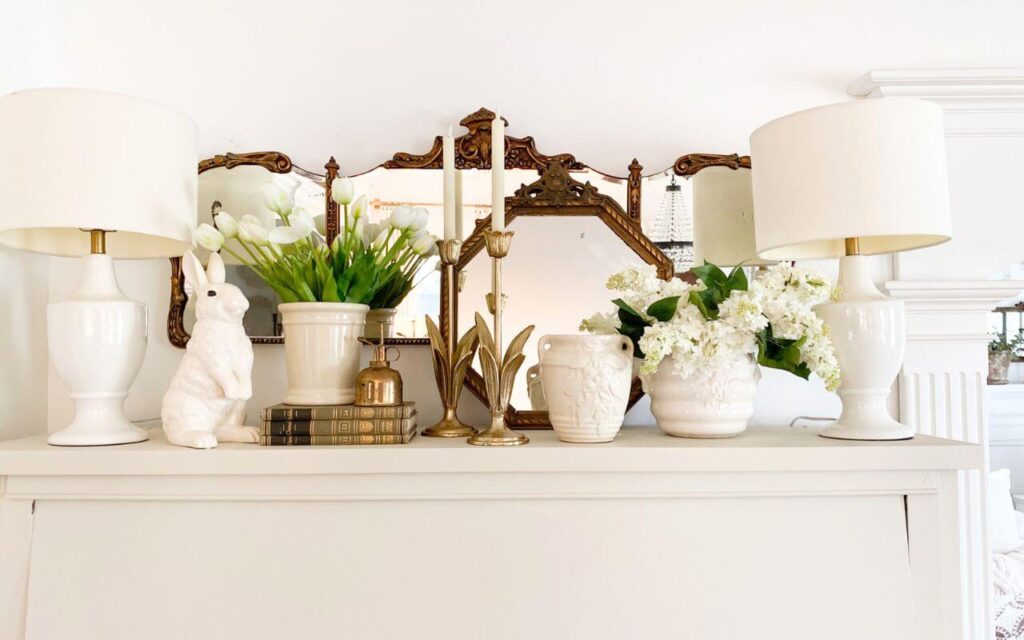 Close view of creamy white painted piano styled with spring florals, a bunny, white lamps and a large gold antique mirror.