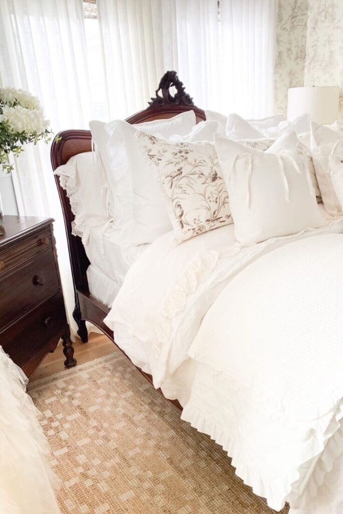 White ruffled bedding layered on an antique bed in a cozy cottage bedroom
