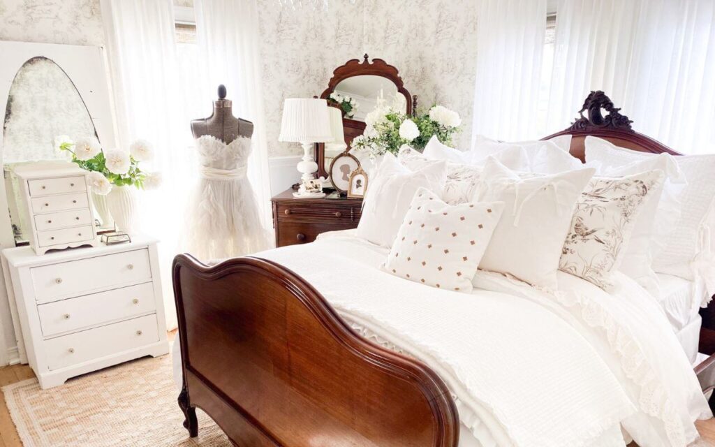 Ruffled bedding ideas in a cozy cottage bedroom with layered white linens and toile wallpaper