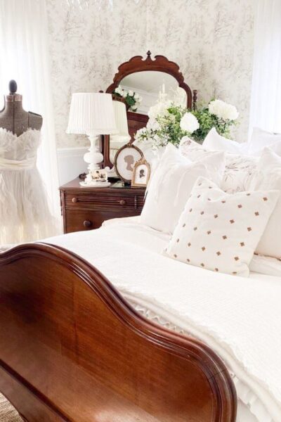 Ruffled bedding ideas in a cozy cottage bedroom with layered white linens and toile wallpaper