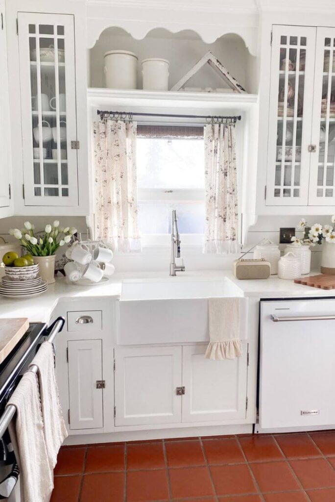 Ruffled floral curtains over the farm sink in a white cottage kitchen.
