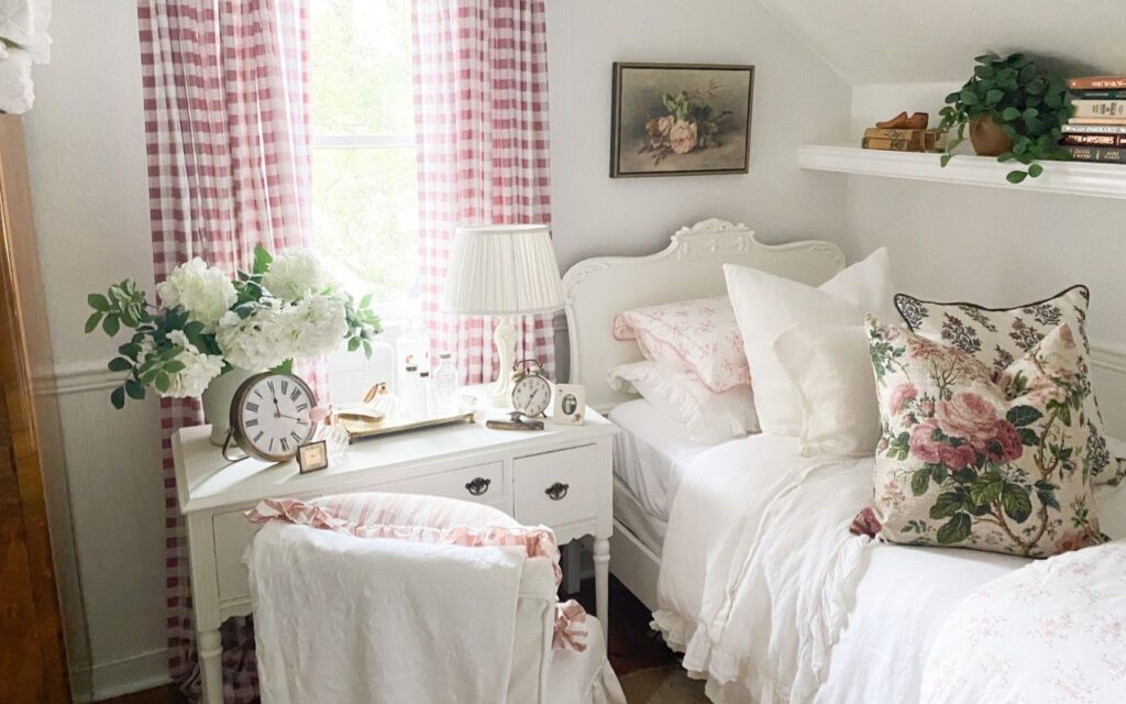 Pink cottage bedroom with gingham curtains, floral bedding, and white antique-style furniture