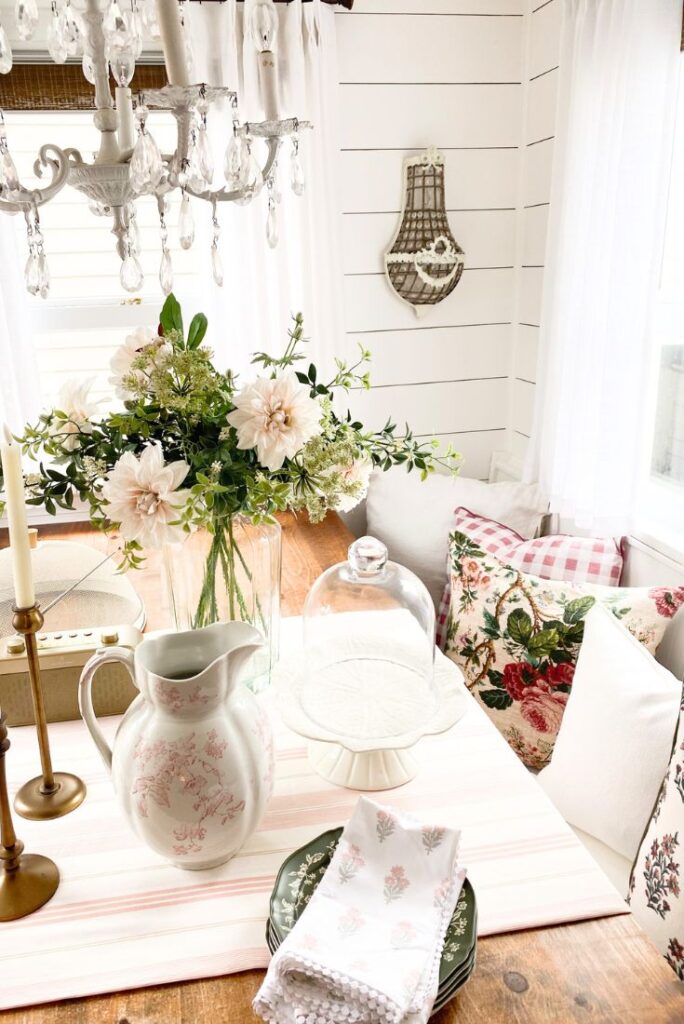 Cottage kitchen decor farmhouse table with vintage pink ironstone pitcher, pink florals and lots of pillows on the farmhouse bench.