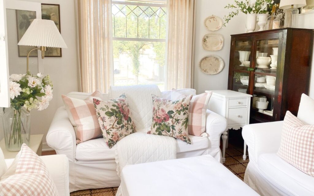 Pink cottage decor with floral pillows and gingham accents on white slipcovered furnitures