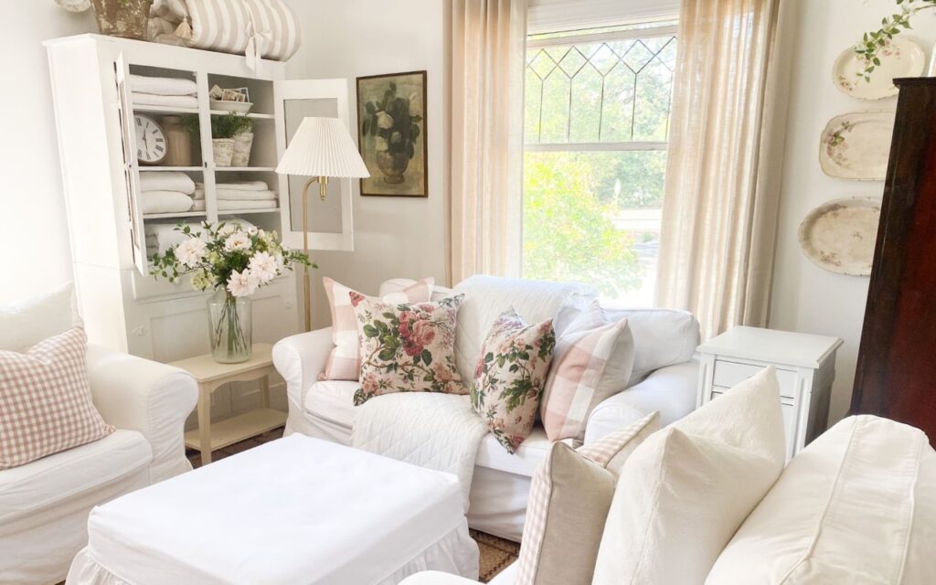 Cottage cupboard, pink buffalo check and pink floral pillows with white slipcovered couches for a cottage living room.